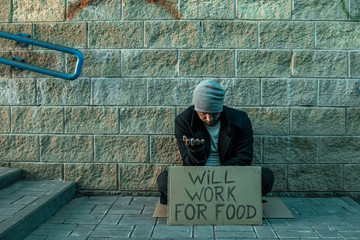 A man, homeless, a man asks for alms on the street with a sign will work for food. Concept of...