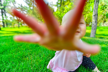 A joyful and happy little girl sits on the green grass and looks around.