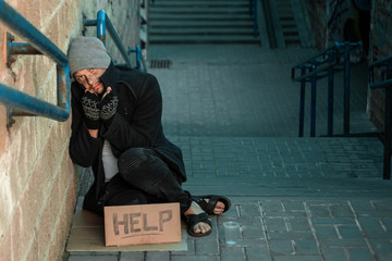 A man, homeless, a man sleeping on a cold floor in the street with a Help sign. Concept of a...