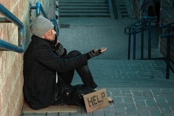 A man, homeless, a man sleeping on a cold floor in the street with a Help sign. Concept of a...