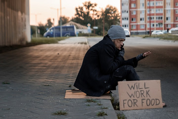 A man, homeless, a man asks for alms on the street with a sign will work for food. Concept of a...