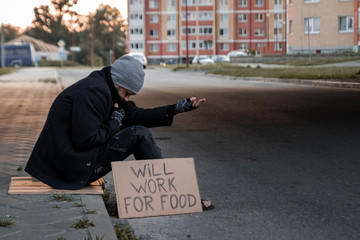 A man, homeless, a man asks for alms on the street with a sign will work for food. Concept of a...