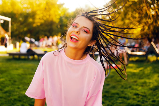 Portrait of a brunette in a park at a festival. A girl in pink clothes, and afro-braids on her head. Girl posing, dancing, dancing, smiling on a sunset background.