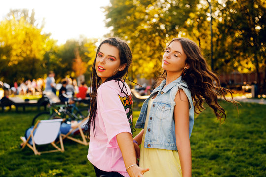 Portrait of a two brunette in a park at a festival. A two sister friends in pink dance.  Girls posing, dancing, smiling on a sunset background.