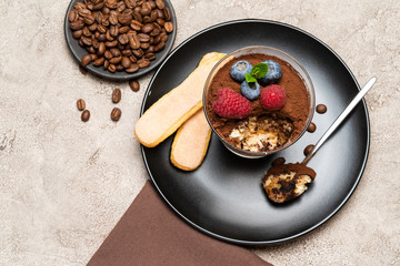 Classic tiramisu dessert portion with blueberries and raspberries in a glass cup on concrete background