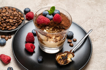Classic tiramisu dessert portion with blueberries and raspberries in a glass cup on concrete background