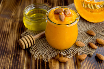 Puree with pumpkin, almonds  and honey in the glass jar on the rustic brown wooden background