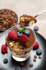 Classic tiramisu dessert portion with blueberries and raspberries in a glass cup on concrete background