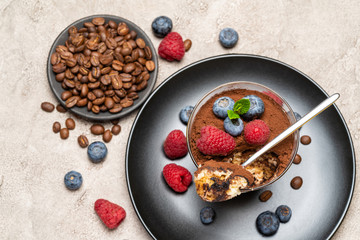 Classic tiramisu dessert portion with blueberries and raspberries in a glass cup on concrete background