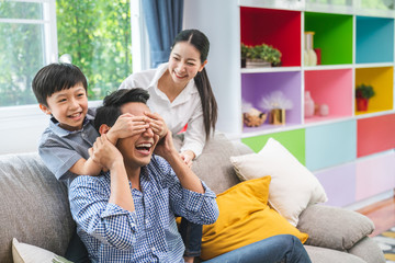 Son blindfolded cute father at home and kids laughing spending time together enjoying on weekend, happy family with father , mother and sons having fun leisure activity in living room