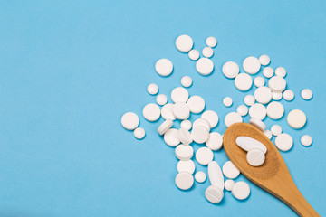 Assorted pharmaceutical medicine pills, tablets and capsules on wooden spoon. blue background