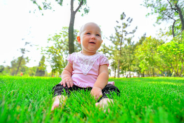 A joyful and happy little girl sits on the green grass and looks around.