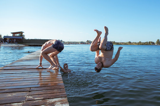 friends jumping from wooden pier in water