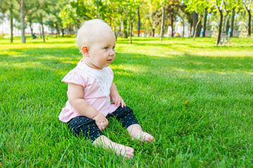 A joyful and happy little girl sits on the green grass and looks around.