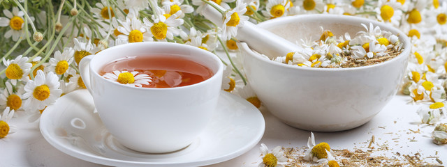 Rural still-life - cup of brewed chamomile tea on the background of a bouquet of daisies, closeup