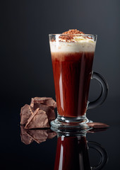 Hot chocolate with whipped cream and pieces of dark chocolate on a dark background.