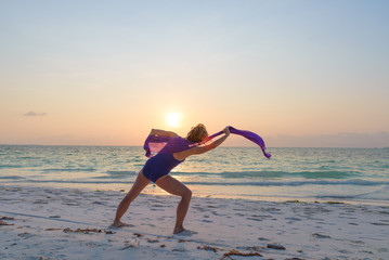 Fototapeta na wymiar Woman performing yoga exercise on sand beach romantic sky at sunset, rear view, golden sunlight, real people