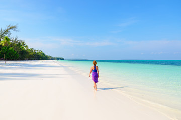 Woman walking on tropical beach. Rear view white sand beach turquoise trasparent water caribbean sea real people. Indonesia Kei Islands Moluccas travel destination.