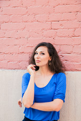 A beautiful brunette woman in a blue blouse posing against a textured pink brick wall. Portrait of a young woman