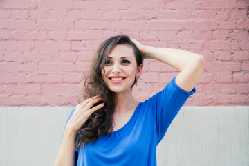 A beautiful brunette woman in a blue blouse posing against a textured pink brick wall. Portrait of a young woman