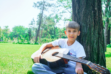 Fototapeta premium A boy with a guitar sits under a tree, sings songs and enjoys nature.