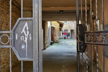 Cast iron gate through which you can see the old courtyard. The surrounding buildings are made of yellow brick. In the yard drying clothes. Lithuania, Vilnus.