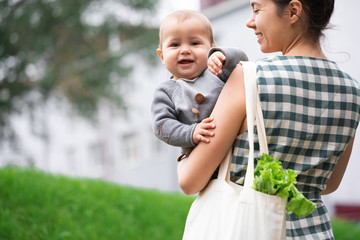 Young mother with baby son walking and shopping fruits and vegetables with reusable cotton Eco produce bag. Zero waste lifestyle concept. Concern for the next generation