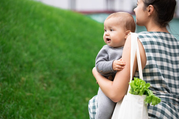 Young mother with baby son walking and shopping fruits and vegetables with reusable cotton Eco produce bag. Zero waste lifestyle concept. Concern for the next generation