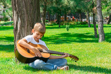 A boy with a guitar sits under a tree, sings songs and enjoys nature.