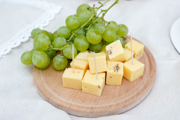 cheese and grapes on a wooden board on white background. picnic food