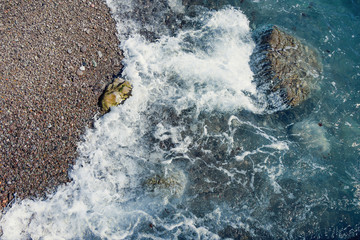 Blue, turquoise sea water washes the coastal pebbles, rocks and boulders. Bright, summer, solar close-up image, selective focus. Purpose for background, Wallpaper, design.