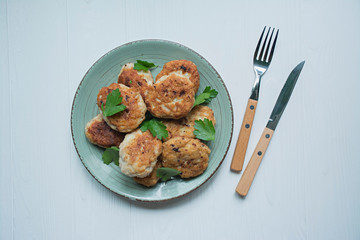 Cutlets with herbs served on a plate on a white wooden background.