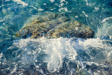 Fototapeta na wymiar Blue, turquoise sea water washes the coastal stone, boulder. Bright, summer, solar close-up image, selective focus. Purpose for background, Wallpaper, design.