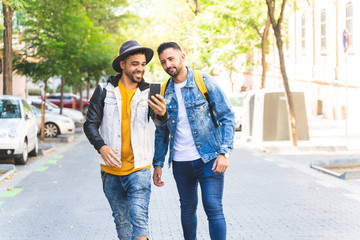 Two Male Friends Walking Together in the Street While Using Cell Phone.