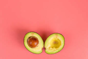 Two halves of avocado with stone on pink background. 