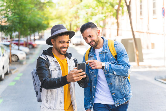 Two Male Friends Walking Together in the Street While Using Cell Phone.
