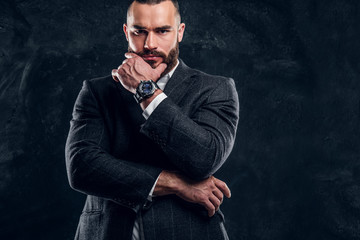 Sceptical bearded man in suit and white shirt is posing for photographer at dark studio.