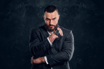 Sucessful serious man is posing for photographer with watch on his fist on the dark background.