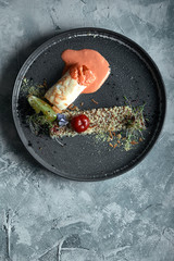 Black cod steak with tomato sauce and buckwheat popcorn, top view on a plate. Copy space, gray background.