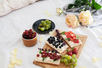 summer breakfast in bed with sandwiches with cheese and berries on bread and flowers