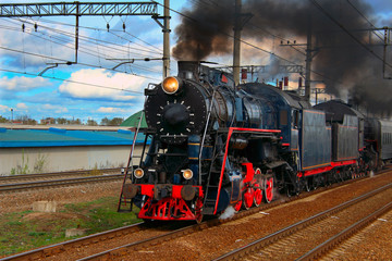 An old steam train in clouds of smoke rides by rail