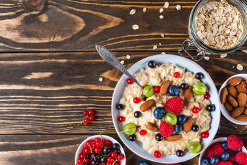 healthy breakfast. bowl of oatmeal porridge with berries, nuts and spoon on rustic wooden table. top view
