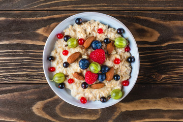 bowl of oatmeal porridge with fresh berries and nuts for healthy diet breakfast on rustic wooden table