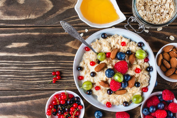 oatmeal porridge with fresh berries, honey and nuts in a bowl on rustic wooden background for healthy diet breakfast