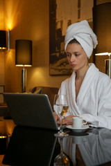 Woman in a white bathrobe working on the laptop, relaxing after a long day, spending a cozy evening alone 