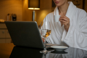 Fototapeta premium Woman in a white bathrobe working on the laptop, relaxing after a long day, spending a cozy evening alone 