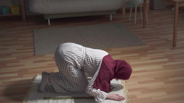 young muslim woman in a traditional scarf sits in a prayer position, raising her hands and praying