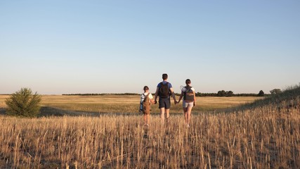 Family of tourists on a journey. Dad with two daughters on camping trip. children and father with backpacks are walking through field. teamwork of tourists. movement towards intended goal and victory