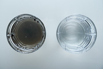top view of two glass glasses, one with crystal clear water, the second with dirty dark water.