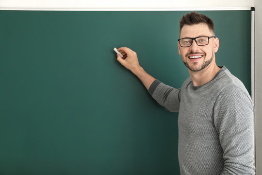 Male teacher writing on blackboard in classroom